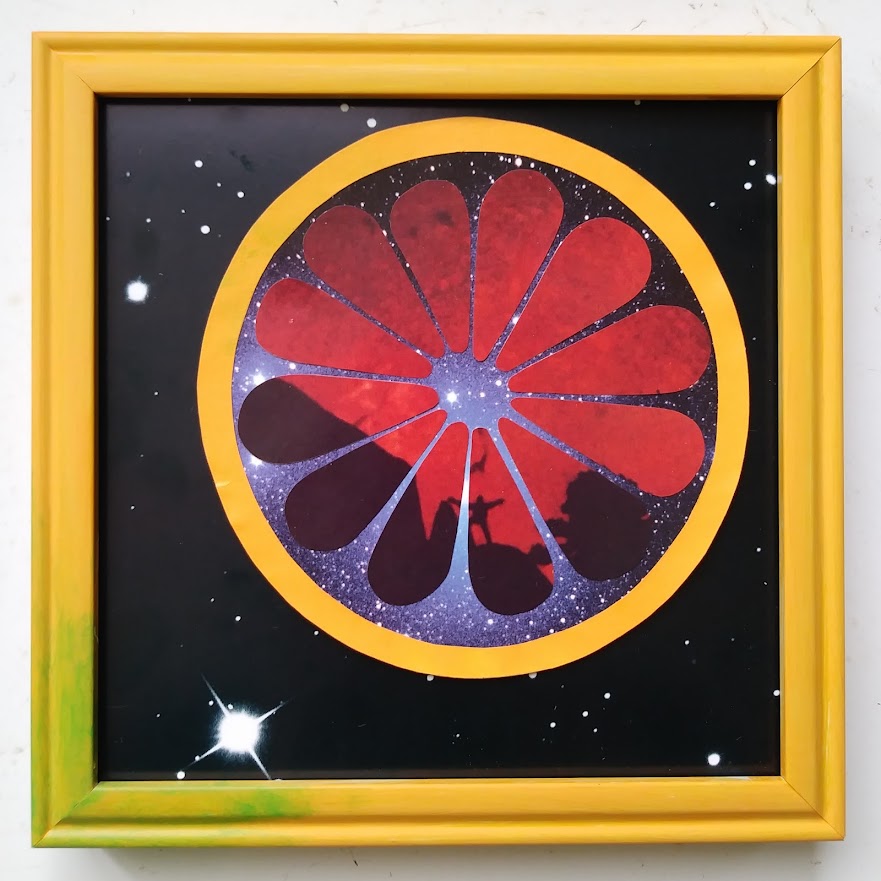 a square collage in a frame painted orange with a green splotch in the bottom left corner to slightly mimic a ripening grapefruit. the background is black space with a scattering of stars and one large bright celestial body in the bottom left corner. there is a large grapefruit off to the upper right corner made like so: an orange paper ring for the peel, a different, busier and brighter photo of starry space for the fleshy part between the peel and the fruit, and 12 wedges cut from a photograph of a tiny silhouette of a person with a huge red sun behind them